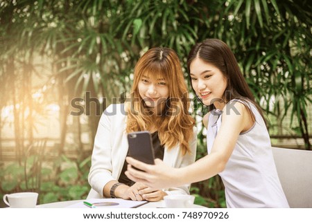 Two pretty young woman taking selfie from hand with smart phone and smiling in the garden, Urban life concept.