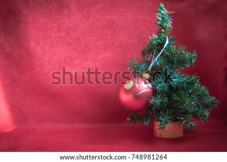 A small Christmas tree on a gold stand is decorated with one big red ball. Preparation for the New Year. Vignetting, daylight.