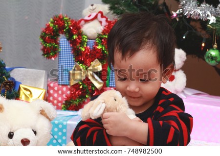 Asian toddler boy feeling happy with his Christmas  present or gift.Boy hug or hold bunny doll in his arm with gentle and care.He looking into the bunny and smiling.Happy Christmas concept. 