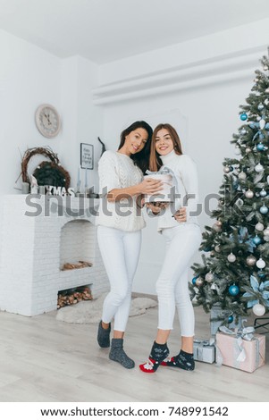 Two happy, stylish and beautiful girl friends presented each other with Christmas gifts and opened them up in the vintage white room.