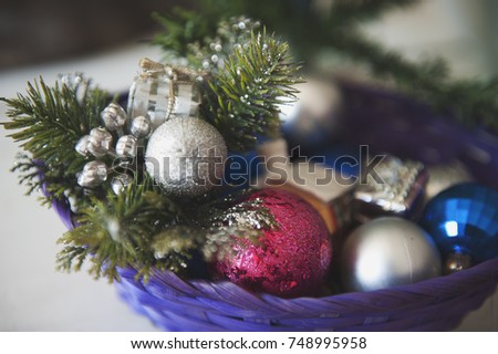 Wattled basket with Christmas decorations on white wooden background. Multi-colored baubles and brilliant tinsel. Close up, concept.