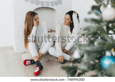 Two happy, stylish and beautiful girl friends presented each other with Christmas gifts and opened them up in the vintage white room.