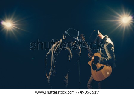 Musician Duo band hand holding the microphone and singing a song and playing the guitar on black background with spot light and lens flare, musical concept
