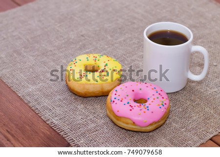 Donuts with icing on the table. Nearby is a mug with coffee. Sweet colored donuts.