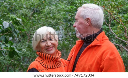 Loving elderly couple with gray hair in orange sweaters against a background of green plants