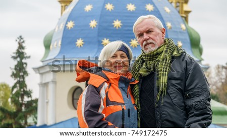 Beautiful elderly couple with gray hair in sports autumn jackets against the background of the dome of the Orthodox church