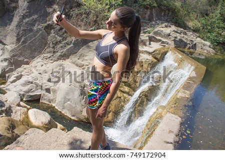 young girl taking self portrait with camera phone on waterfall. Travel and technology