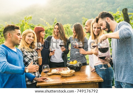 Group of happy friends having fun outdoors drinking red wine - Young people eating local fresh food at grape harvesting in farmhouse vineyard winery - Youth friendship concept on a vivid warm filter
