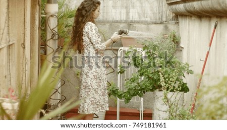 Pretty long-haired girl in cute floral dress watering plants in her patio garden