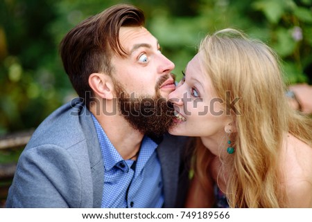 A picture of a young romantic couple with flowers in the city. A girl bites a guy for his beard.