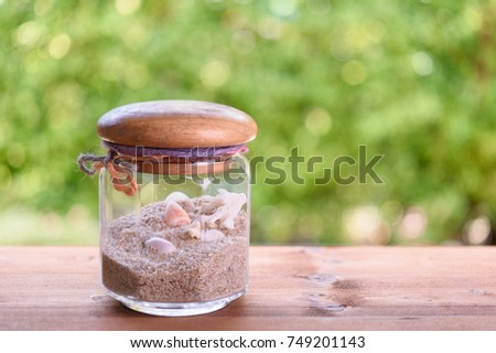Seashells and sand in glass jar on wood table with green blurred background