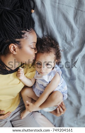 Portrait of pretty African woman lying on bed with her baby daughter.
