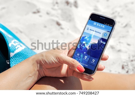 One young woman resting in the beach and holding a smartphone with mobile banking  application on the screen.