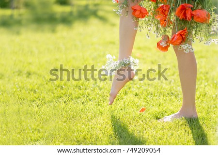 Spring is coming concept. Beautiful woman legs barefoot wearing floral dress waling on a sunny meadow