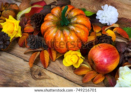 Thanksgiving orange pumpkin, apple, pine cones and yellow roses wreath on the wooden background, close up