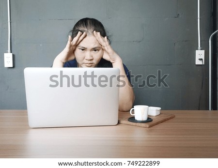 Portrait of stressful woman while sitting in front of her notebook with cup of coffee against grey wall/background