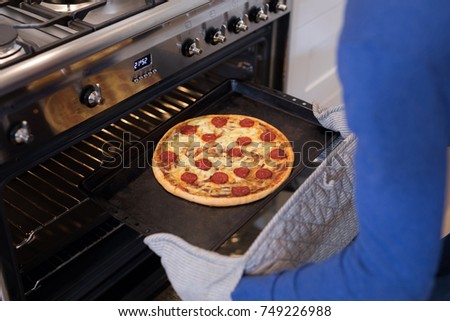 Man putting pizza into oven in kitchen at home