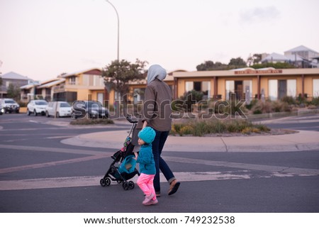 A young Muslim woman with his daughter walking at the street with blur background.