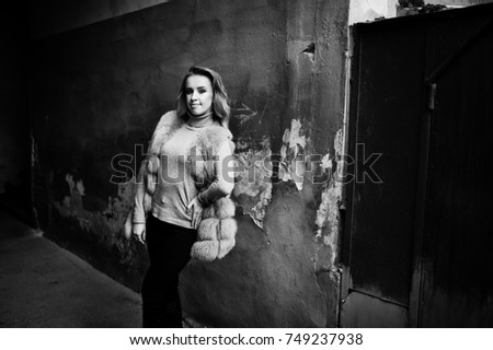 Blonde girl at fur coat posed against old orange wall.
