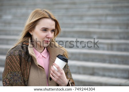 Cute blonde in the city drinking coffee on the stairs
