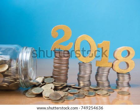 2018 New year saving money and financial planning concept. Gold wooden number 2018 on stack of coins w/ glass of coins or piggy bank. Creative idea for business growth, tax payment and investment.