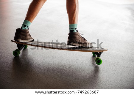 Man`s legs in brown sneakers and blue socks standing on a longboard with green wheels