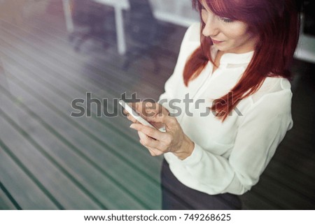 Businesswoman with smartphone in her office working.