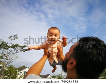 Father holding his baby daughter in the air with both hands, against the blue sky; the concept of freedom, strength, parenthood, happiness and family life.