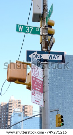 Collection of street signs at West 37th Street and 10th Avenue in New York City, with traffic lights beyond