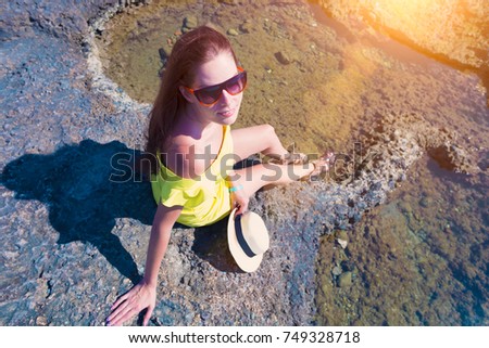 Young beautiful woman in yellow dress sitting on the rocks on the beach or the ocean top view