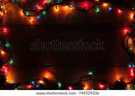 Glowing Christmas garland forms a frame  on brown wooden board as background.