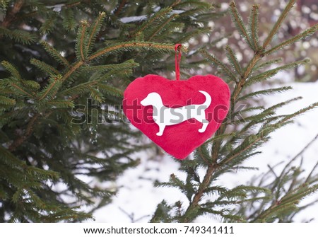 Paper dog figure on red decorative plush heart on fir-tree green branches.