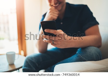 Happy smiling man using his smartphone device at home, hipster guy typing an sms message via cellphone, sunny day