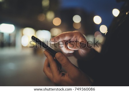 Closeup of male hands using smartphone device at night , bokeh lights on the background, communication and social networks concept