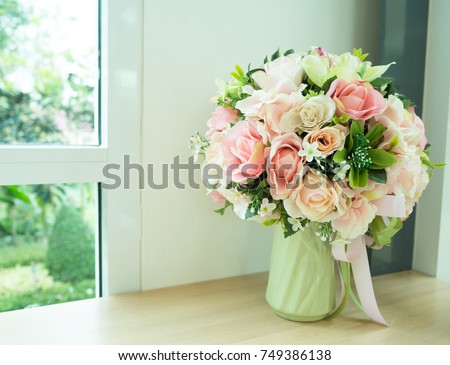 Artificial roses in the vase on the table and mirror window.