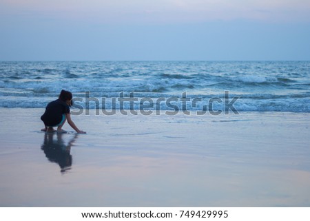 silhouette of The Adorable Little girl playing on the beach and her hand touch the sand at the sunset time.