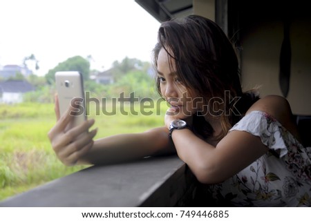 young beautiful Asian girl taking selfie picture with mobile phone camera smiling happy sitting outdoors at coffee shop in a beautiful nature background smiling happy and sweet