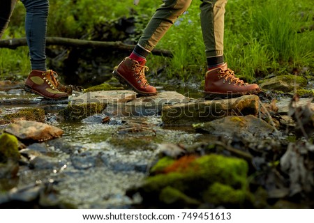 Woman hiker crossing a small forest stream in a close up low angle view of her feet in leather boots on natural rock stepping stones Royalty-Free Stock Photo #749451613