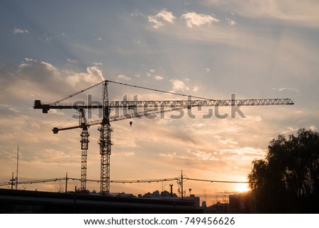 Industrial construction cranes and building silhouettes against the sunset sky 
