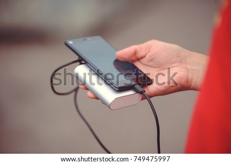 the man is holding the phone and the charger. Powerbank and smartphone in hand. Power-saving device power bank smartphone. Royalty-Free Stock Photo #749475997