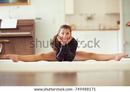 Young pretty girl has training gymnastics at home in black leotard in white interior