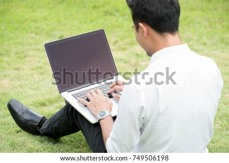 Man on white shirt use laptop with black blank screen sit on green grass