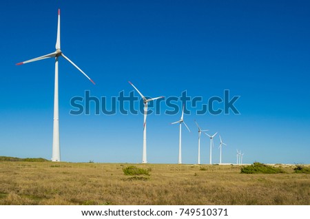 Great concept of renewable, sustainable energy. Wind field with wind turbines, producing aeolian energy under blue sky. Royalty-Free Stock Photo #749510371