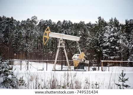 Horizontal view of a pump jack in the oilfield situated in the beautiful winter forest. Environmental pollution. Oil and gas concept.