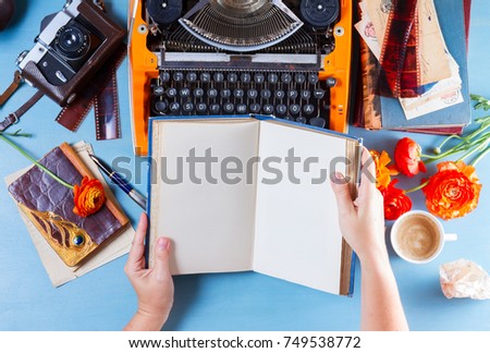 Workspace with orange retro typewriter, someones hands holding open book with copy space