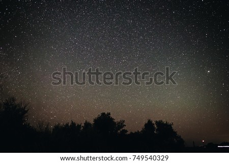 Background of bright starry night sky with lights upon on it and silhouette of trees.