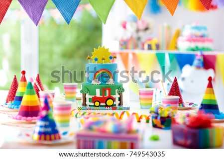Kids birthday party decoration. Colorful cake with candles. Farm and transportation theme boys party. Decorated table for child birthday celebration. Rainbow cake for little boy. Balloons and banners. Royalty-Free Stock Photo #749543035