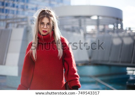 Melancholic portrait. Young girl in a red sweater on a background of skyscrapers, disheveled hair.