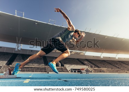Runner using starting block to start his run on running track in a stadium. Athlete starting his sprint on an all-weather running track. Royalty-Free Stock Photo #749580025