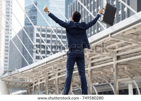 Asian businessman holding the briefcase and raising arms standing in downtown with job to success,city background